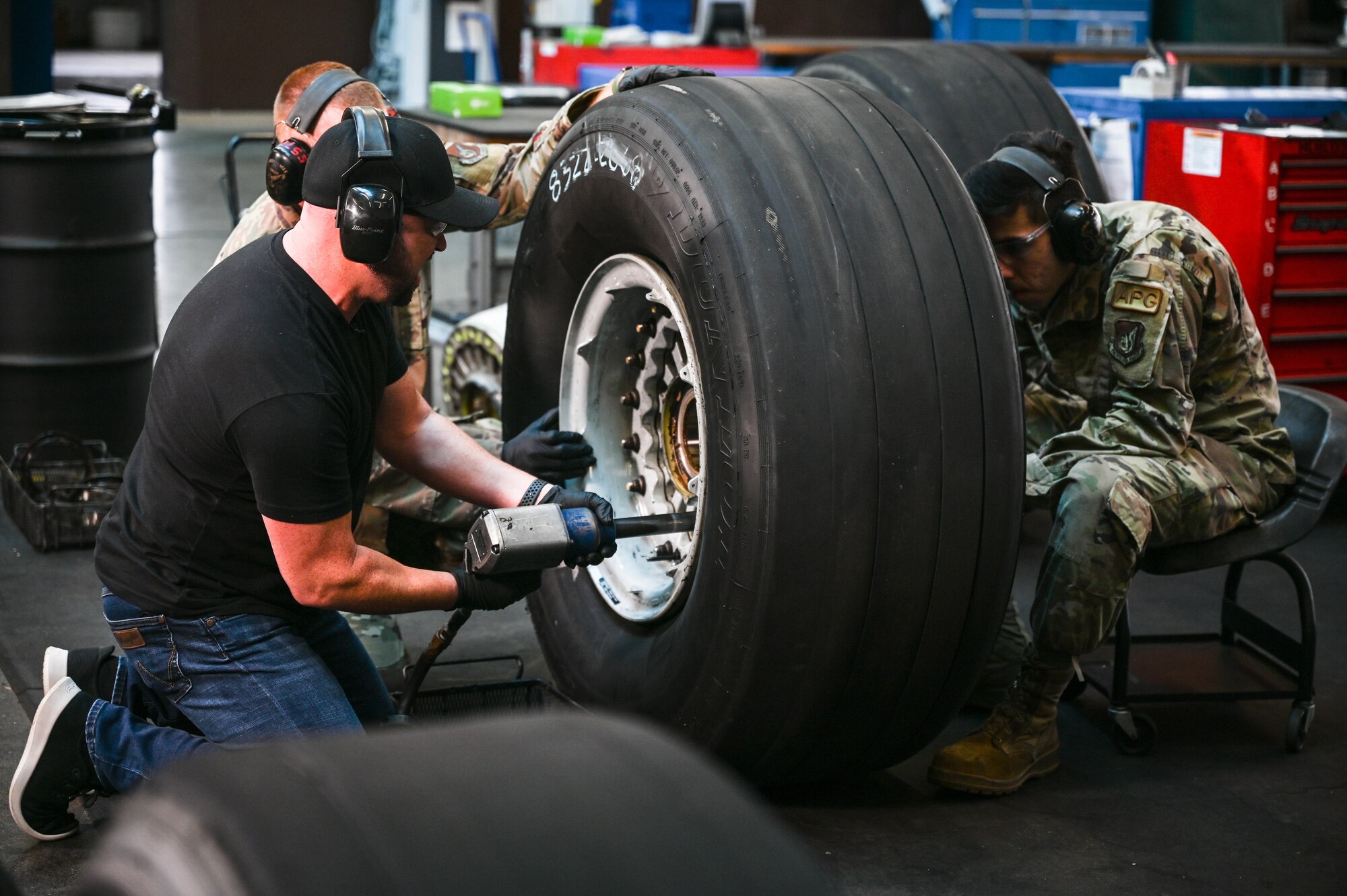 Cody Alan, Country Music Television Radio host and executive producer, detaches bolts from a C-17 Globemaster III tire with Master Sgt. Michael DePue, 15th Maintenance Squadron flight chief, and Airman Joshua Garcia, 15th MXS wheel and tire technician, while filming for CMT’s Hot 20 Annual Holiday Salute to the Troops at Joint Base Pearl Harbor-Hickam, Hawaii, Nov. 29, 2021. Airmen from the aircraft structural, metals technology, and wheel and tire sections from the 15 MXS highlighted how they enable the C-17 to carry out airlift missions. (U.S. Air Force photo by Staff Sgt. Alan Ricker)