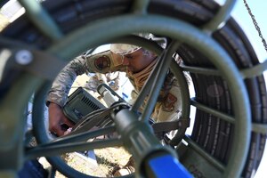 A cyber technician kneels behind a high frequency whip antenna