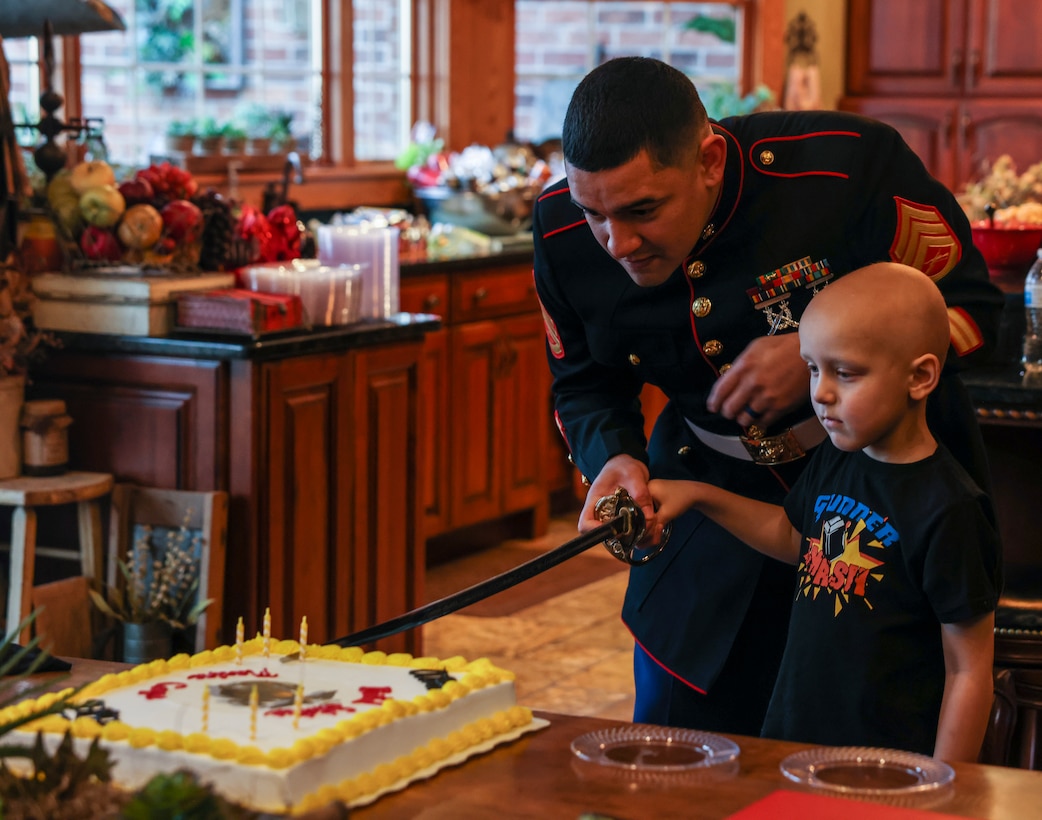 U.S. Marine Corps Staff Sgt. Christophe Decasanova, recruiter with Recruiting Station St. Louis, helps Gunner Sadler cut a cake in their home in Bloomington, Ill. on Dec. 18. The Marine Corps coordinated with the Saddler family to conduct the ceremony in honor of Gunners strength and tenacity as he faces the road forward, guided by the Make-A-Wish foundation. Ryan is a Marine Corps veteran who wanted to share a Marine Corps tradition with his son.  (U.S. Marine Corps photo by Lance Cpl. Tyler M. Solak)