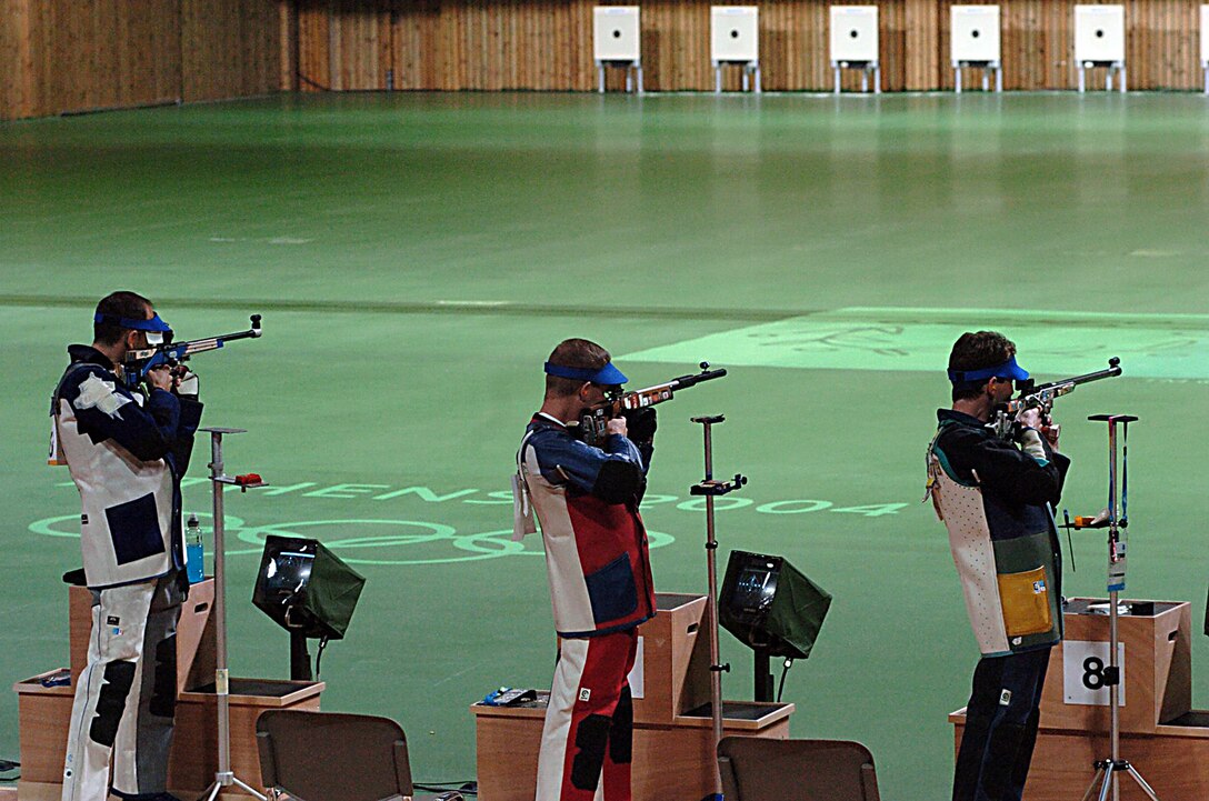 Three competitive shooters aim their rifles downrange.