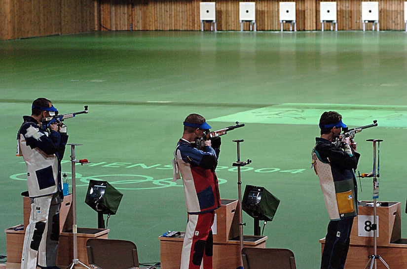 Three competitive shooters aim their rifles downrange.