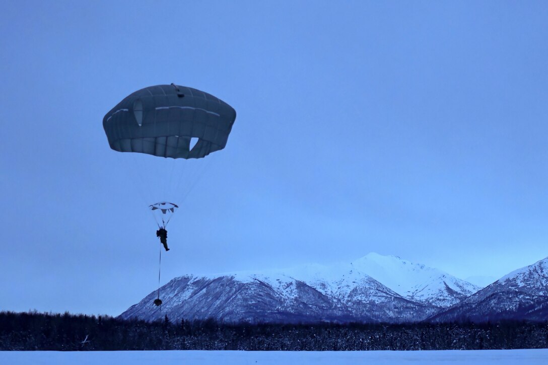A soldier free falls with a parachute in front of a snowy mountain.