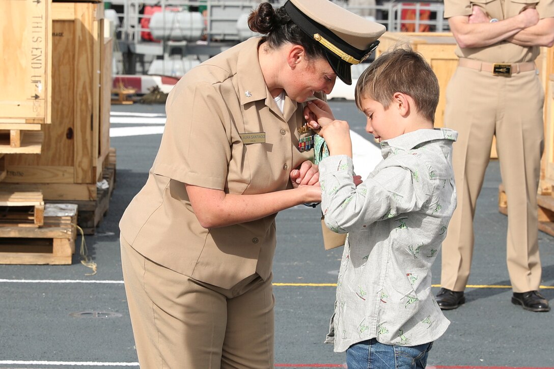 A son pins a sailor during a promotion ceremony on a ship.