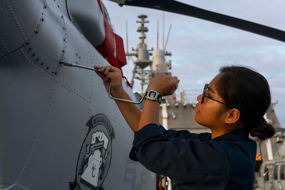 A sailor performs maintenance on an aircraft aboard a ship at sea.