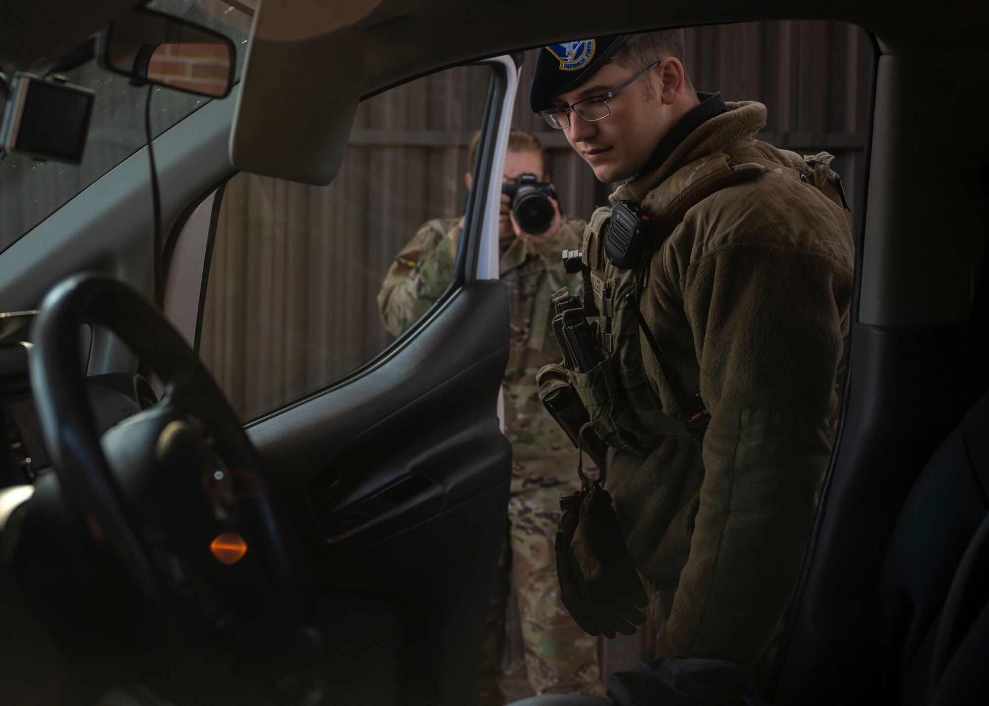 Airman 1st Class Sven Fuller, 4th Security Forces Squadron entry controller, inspects a vehicle at a check point as his younger sister, Airman 1st Class Sabrina, 4th Fighter Wing public affairs specialist, takes his photo at Seymour Johnson Air Force Base, North Carolina, Dec. 7, 2021.