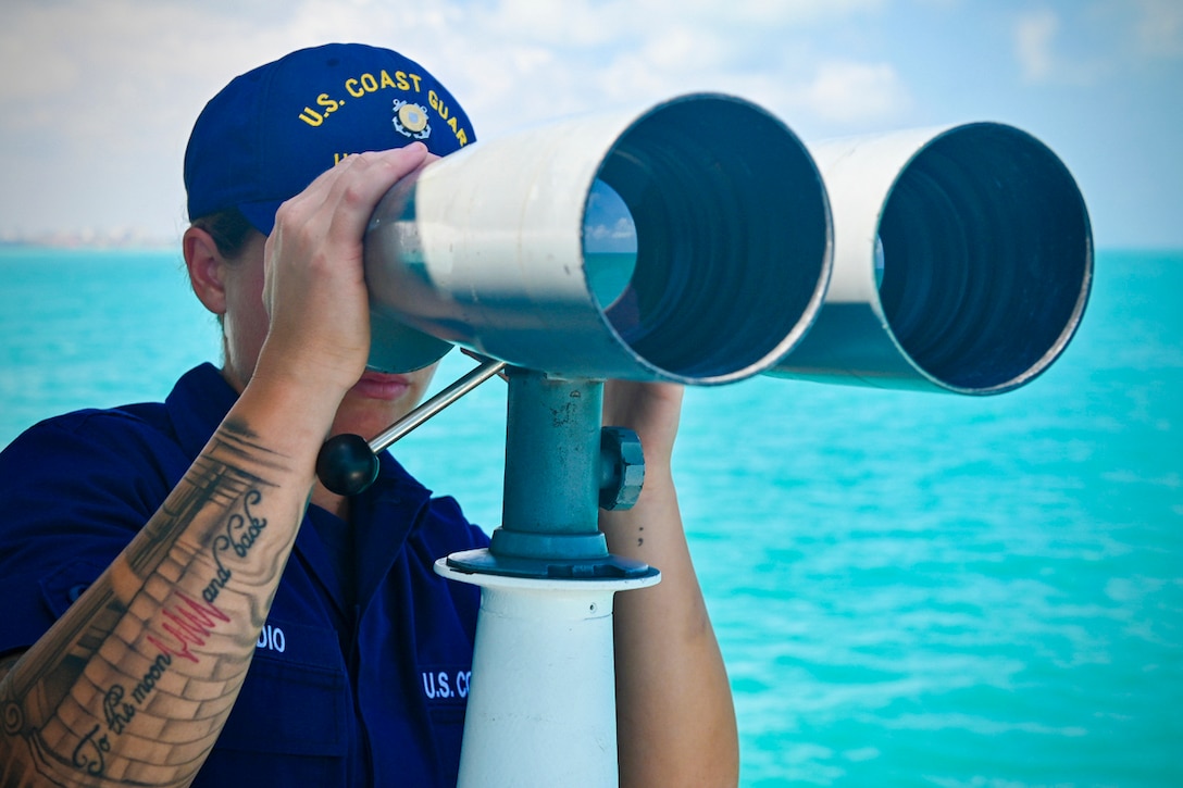 A Coast Guardsman looks through large binoculars.