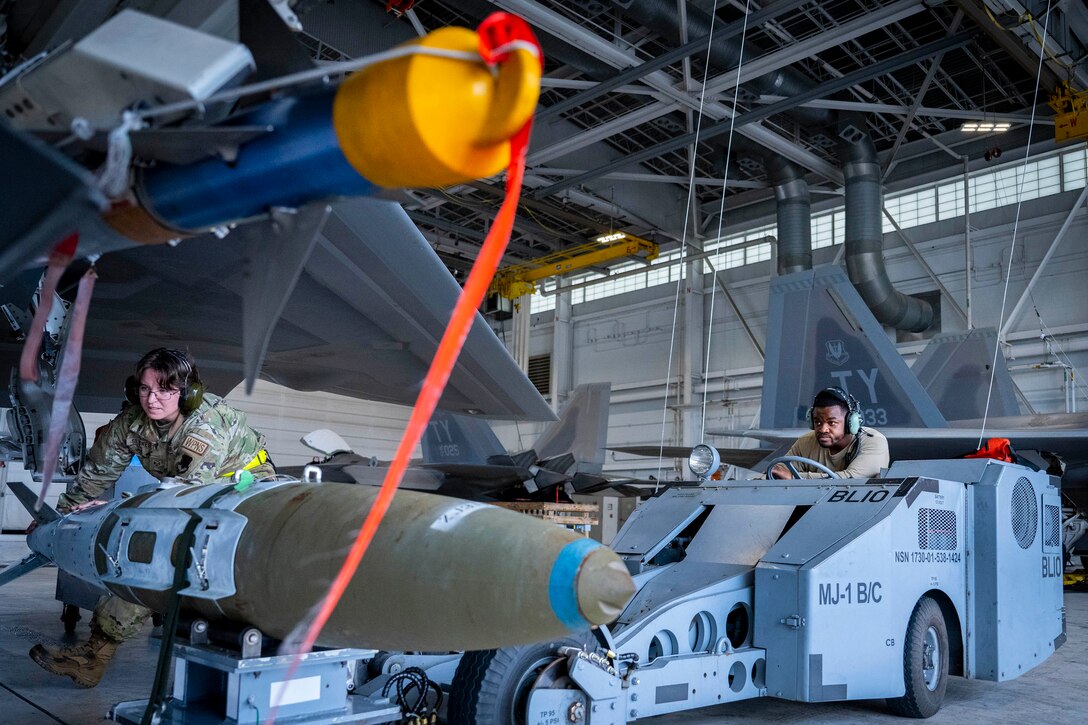 Two airmen move a munition using military equipment.