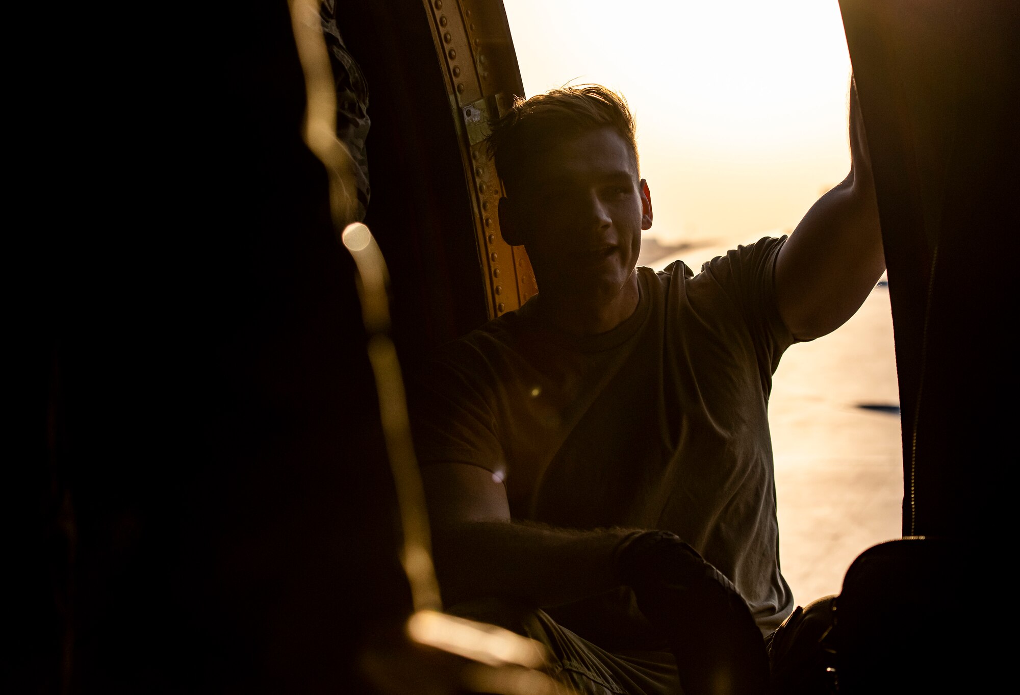 Male service member sits in door way of a wing hatch of an airplane.