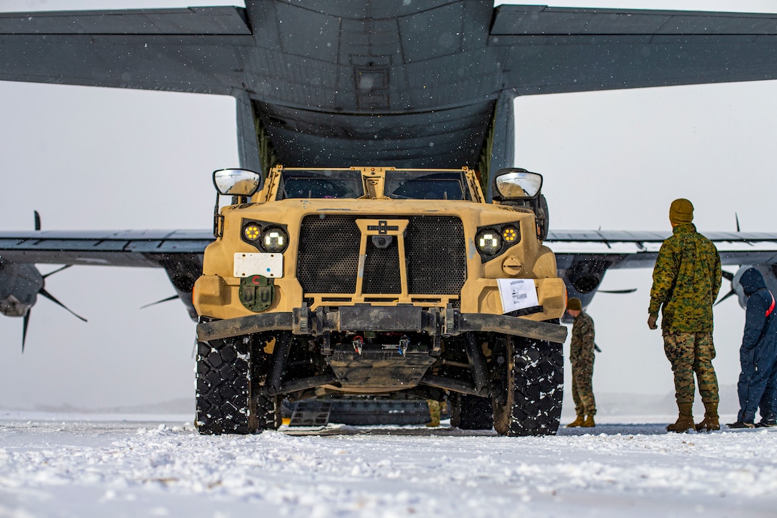 Marines back a vehicle into an aircraft on a snowy flightline.