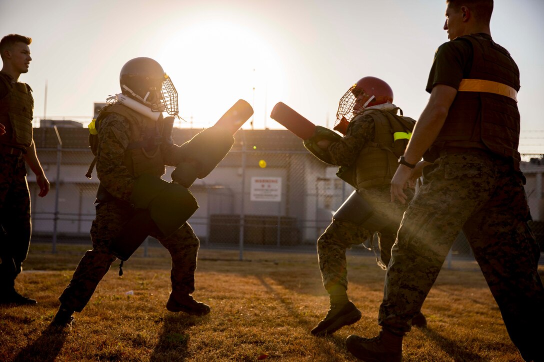 Marines holding pugil sticks wearing protective gear compete in field.