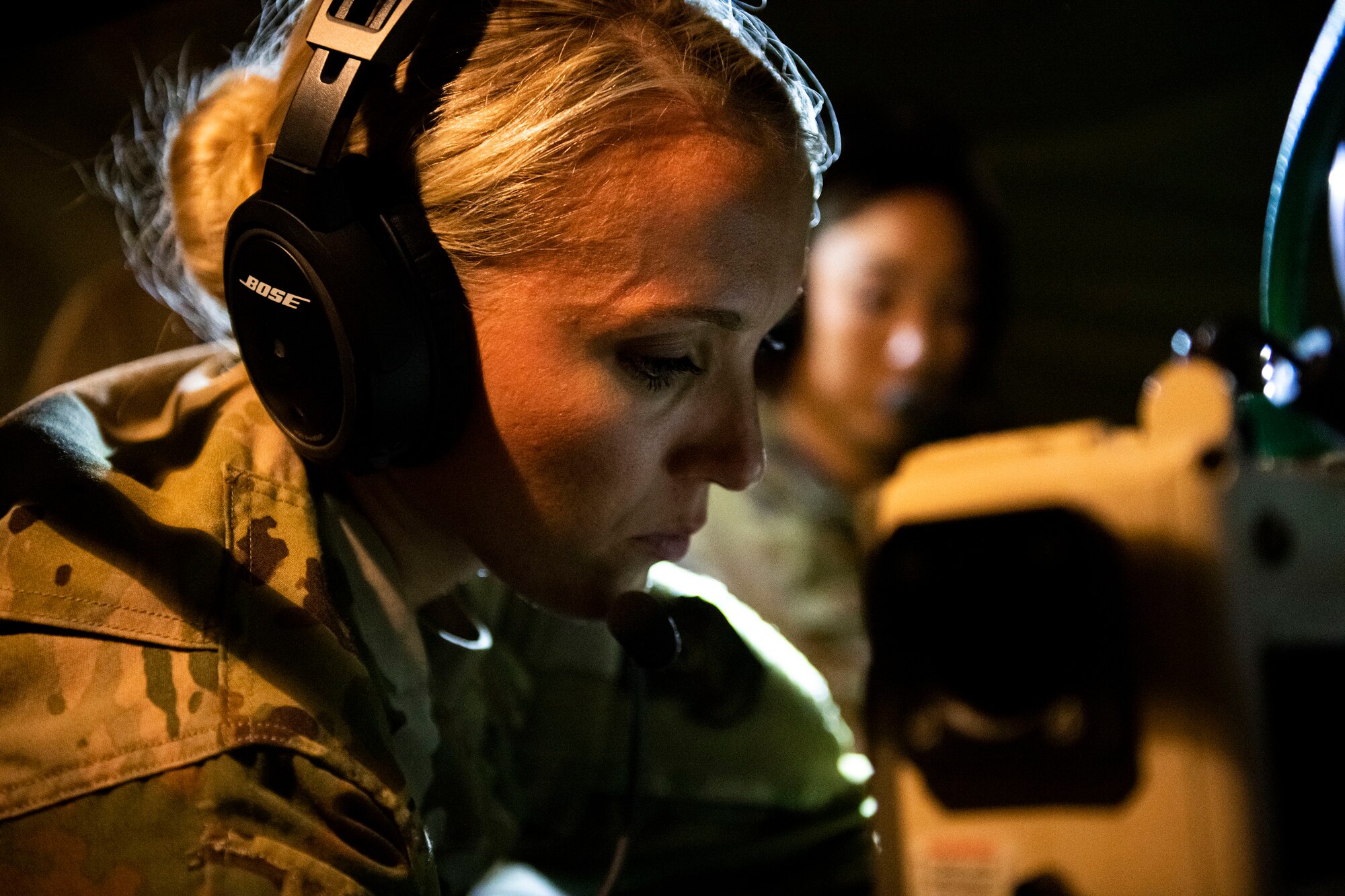Female service member works on medical equipment with headset on.