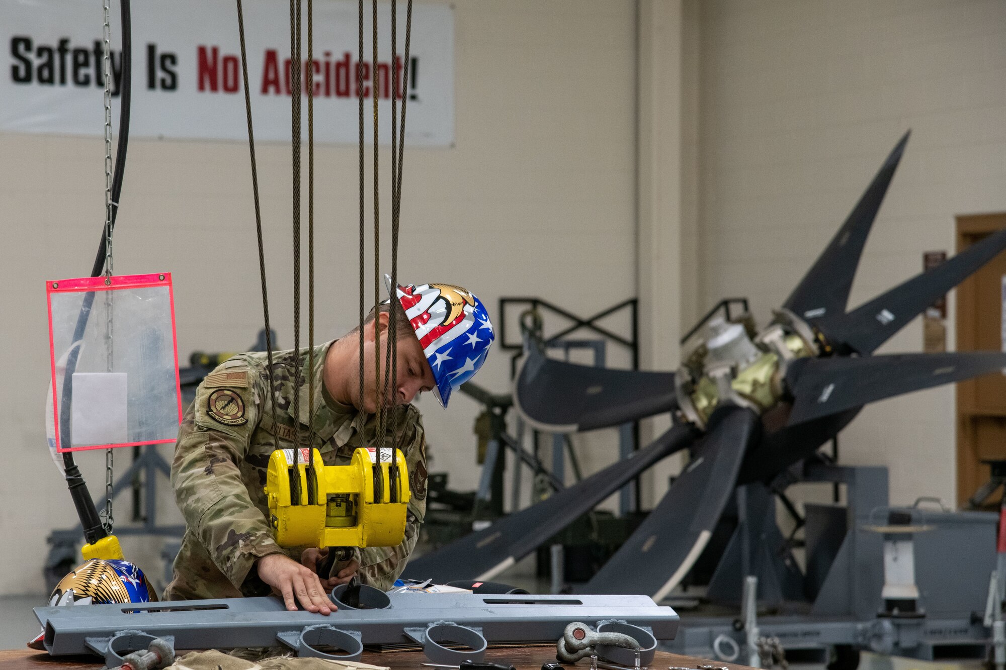 An Airman removes a 4-ringd bar from a hoist. large propeller in the background.