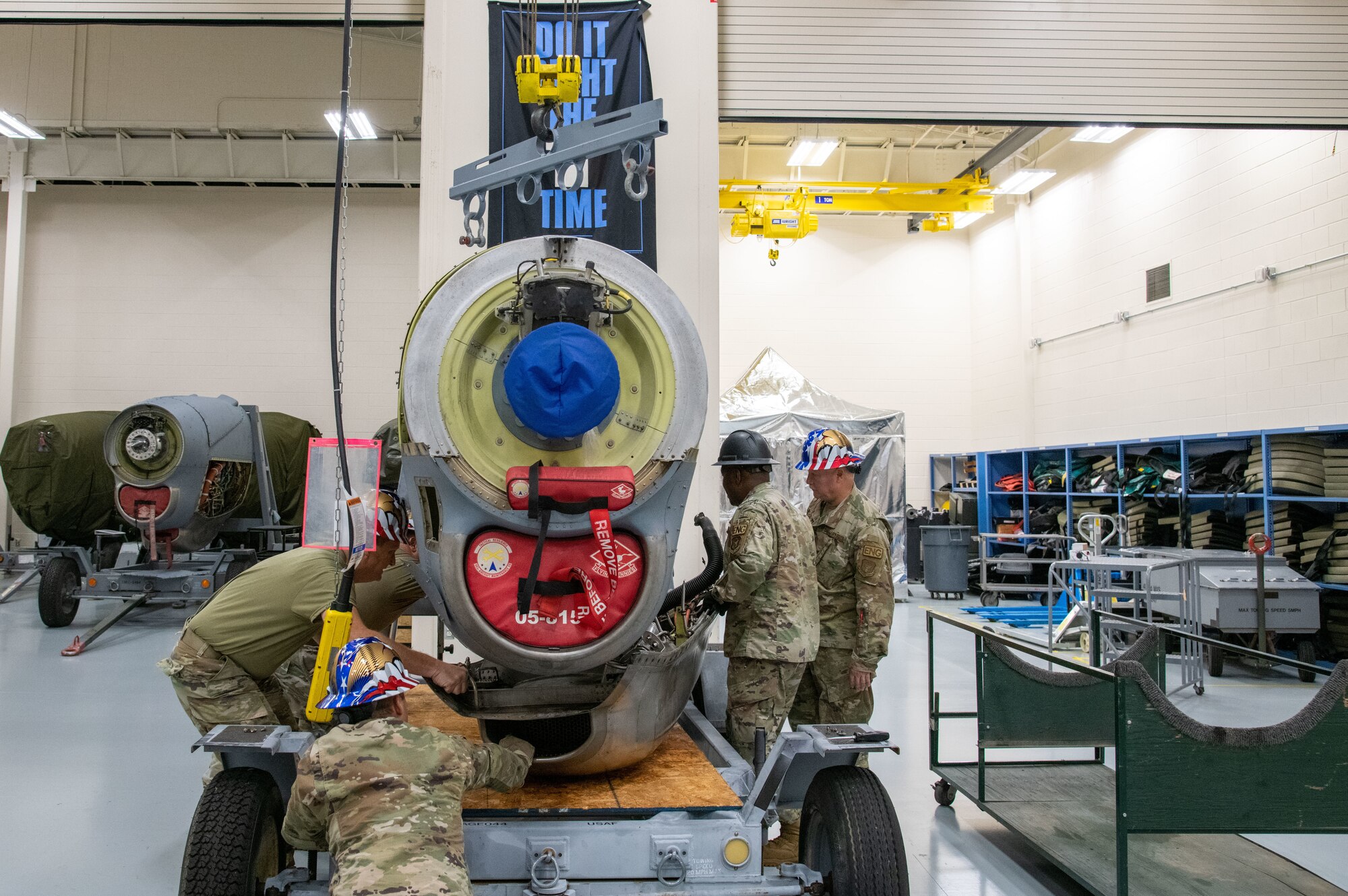 A c-130 engine is center, 3 men are on the left, 2 on the right, removing the pan from under.