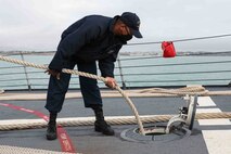 Personnel Specialist 2nd Class Deshawn McGowan, assigned to the Arleigh Burke-class guided-missile destroyer USS Ross (DDG 71), stows a mooring line as the ship leaves port at Naval Station Rota, Spain, Dec. 27, 2021. Ross, forward-deployed to Rota, Spain, is on its 12th patrol in the U.S. Sixth Fleet area of operations in support of regional allies and partners and U.S. national security interests in Europe and Africa. (U.S. Navy photo by Mass Communication Specialist 2nd Class Claire DuBois/Released)