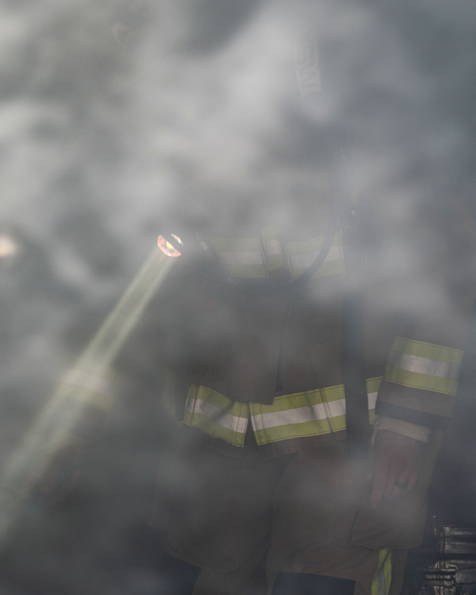 A fireman shines a light through a smoke filled room.