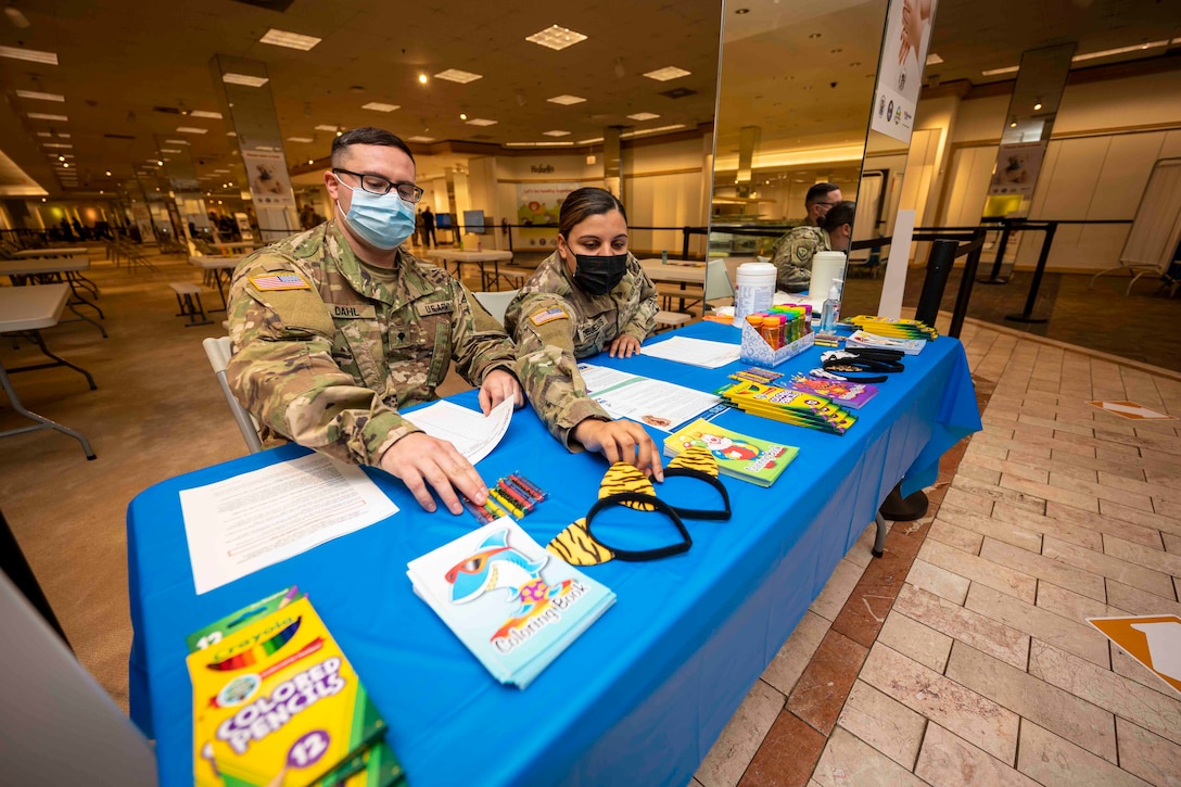 Two soldiers sit at a table with papers, colored pencils and crayons.