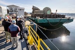 People observe a barge loaded with large pieces of industrial scrap metal.