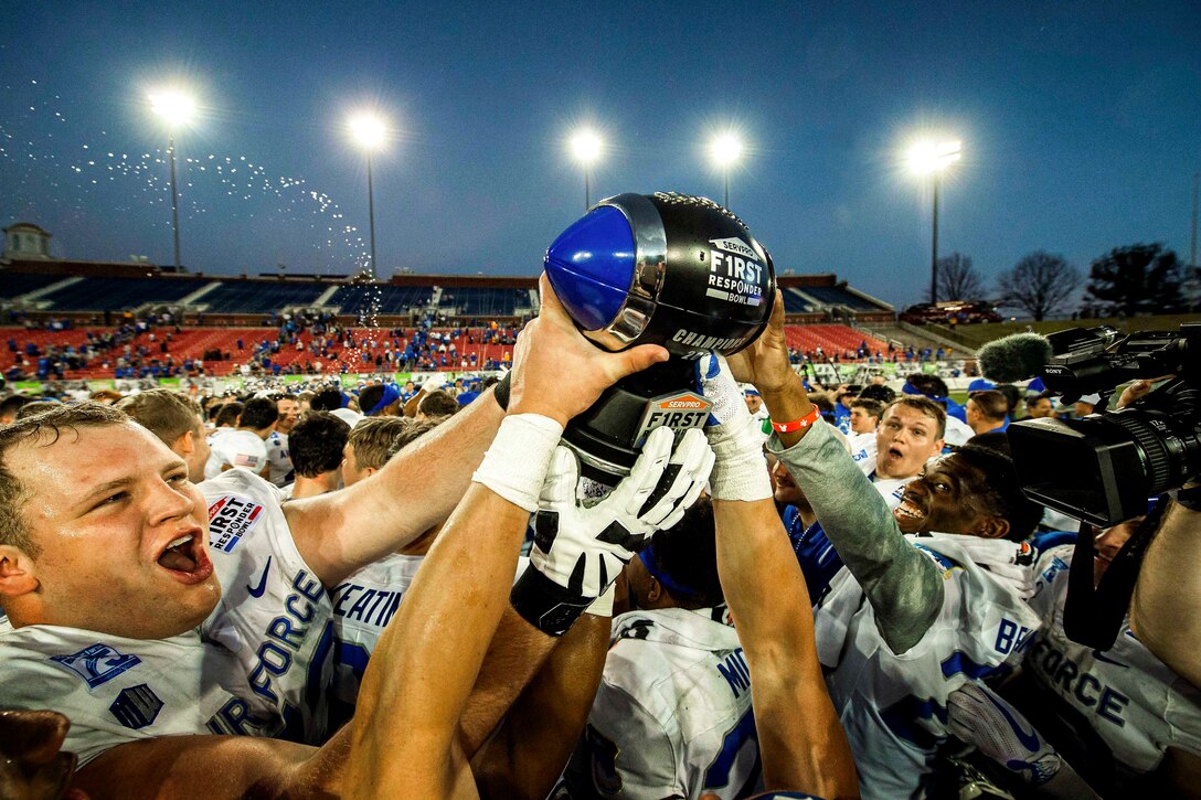 Air Force football players gather in a circle and hold a trophy.