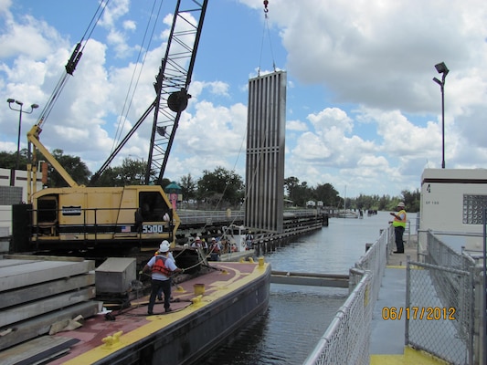 Before major lock maintenance and repairs can take place, the lock must be dewatered so that inspections and repair work can be done in relatively dry conditions. Using a barge-mounted crane, the crane operator and rigging crew set a needle dam girder (I-beam) in place in notches built into the lock chamber wall. Then, they place large metal panels known as “needles” against the I-Beam to form a wall called a “needle dam.” (USACE Jacksonville District photo from a 2012 maintenance repair project at the St. Lucie Lock in 2012)