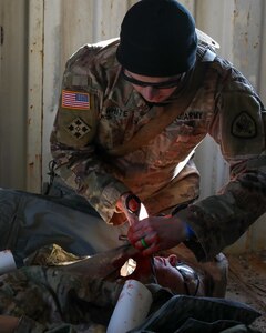 A soldier gives first aid to a simulated casualty laying on the floor