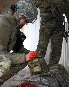 A soldier gives first aid to a simulated casualty laying on the ground