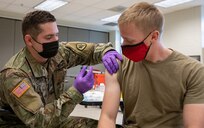 A medical soldier gives a shot to another soldier