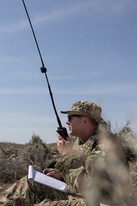 A soldier communicates through a radio while observing enemy activity