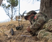 A Soldier lays on the ground and uses radio