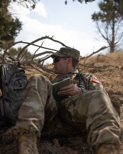 A soldier sits on the ground and takes notes