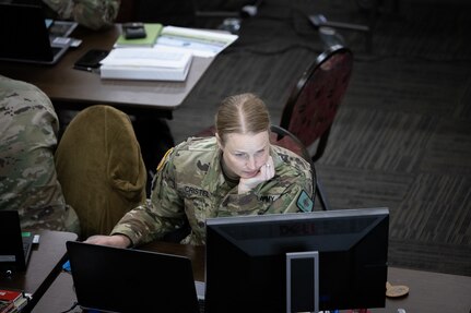 Female soldier sit at desk looks at computer screen