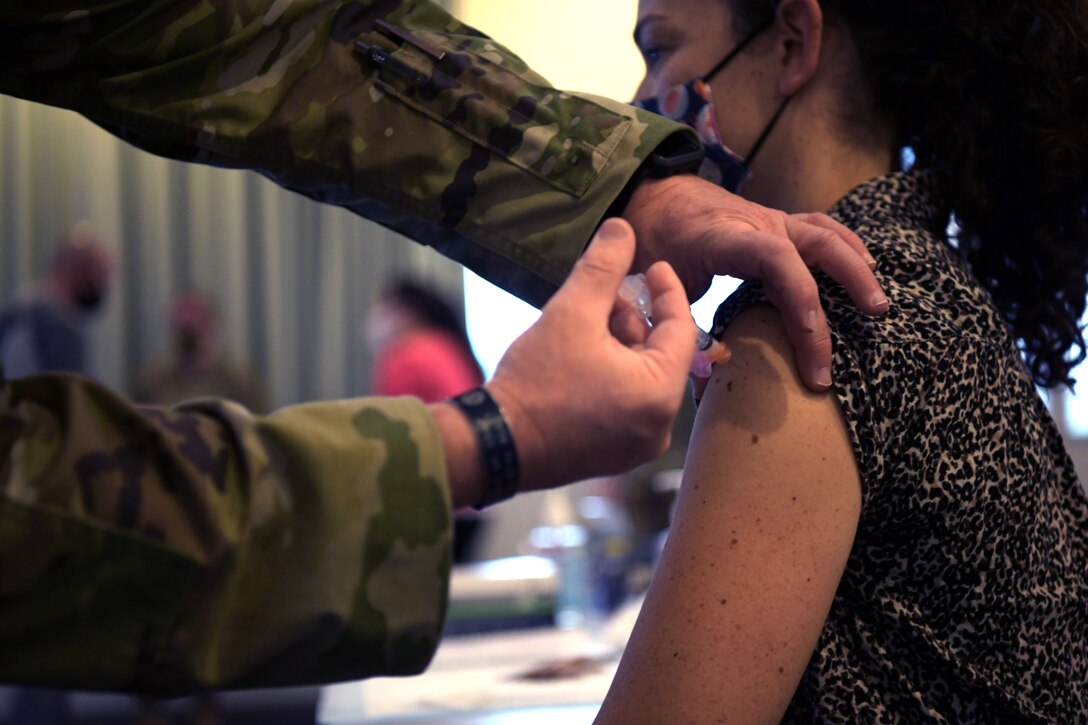 A woman wearing a face mask is given a COVID-19 vaccine by a soldier.