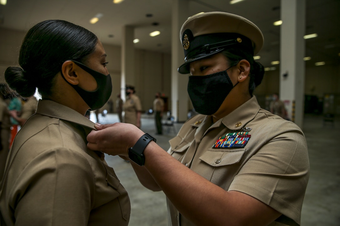 A service member puts a pin on a sailor’s collar.