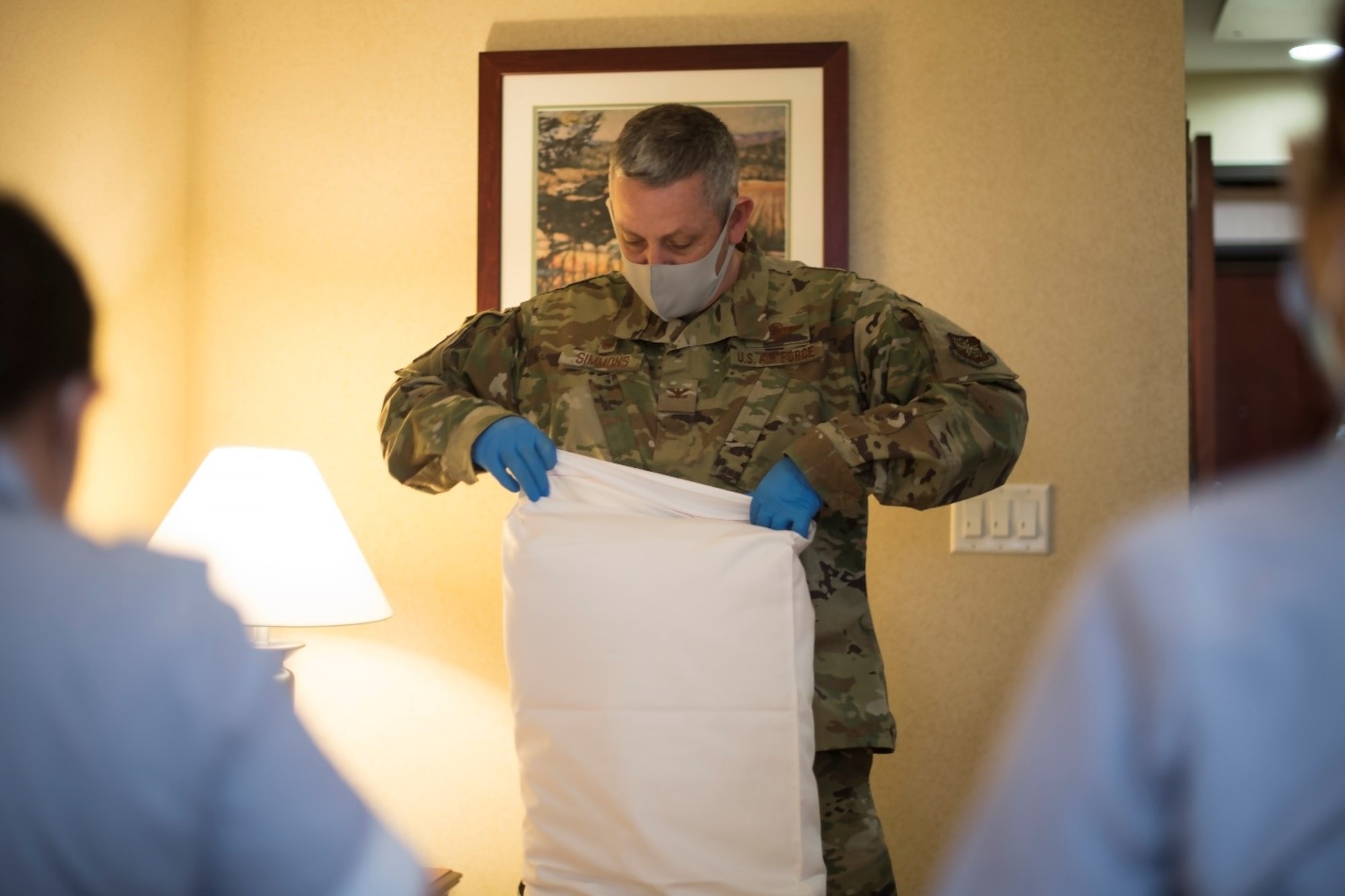 A man in a military uniform puts a pillow in a pillowcase while two room attendants look on