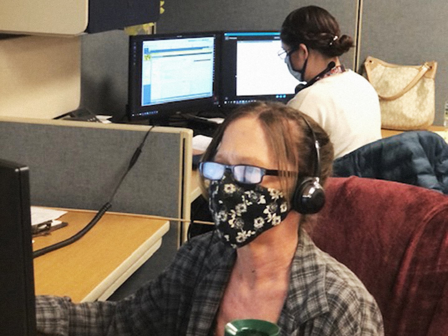 Woman wearing eyeglasses, face mask and plaid shirt sits in front of a computer screen with a headset.