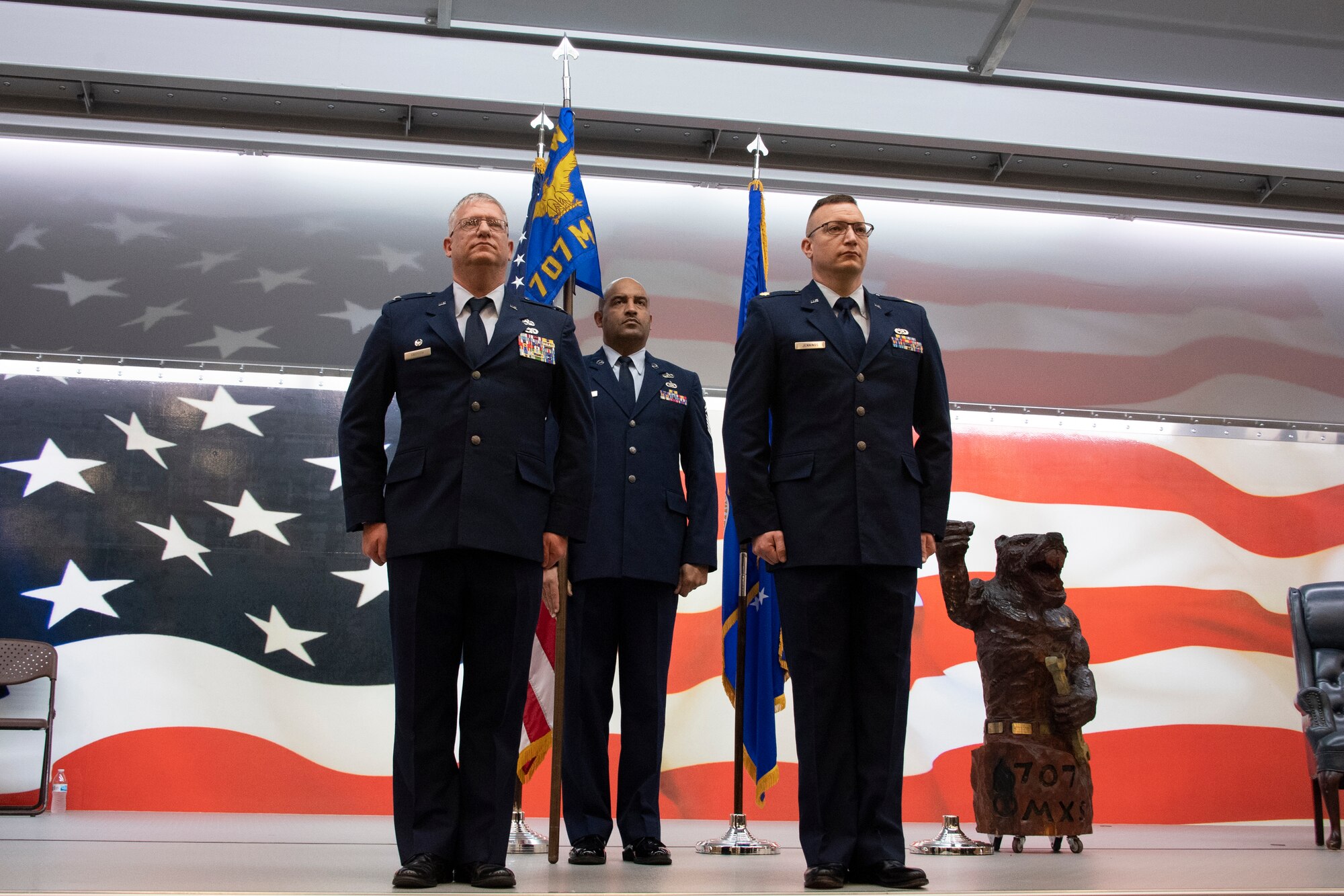 Photo of Airmen standing at attention with U.S. flag in background. One holds a unit guidon.