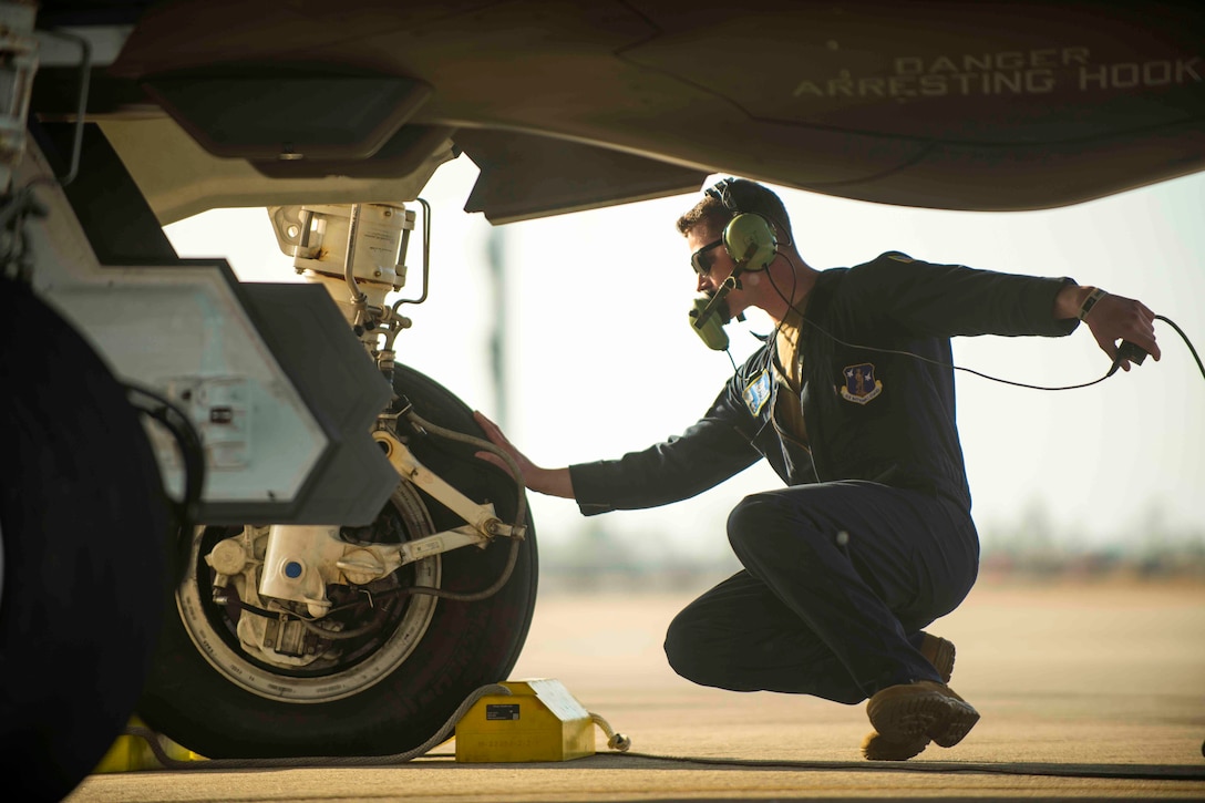 An airman kneels underneath an aircraft while touching a tire.