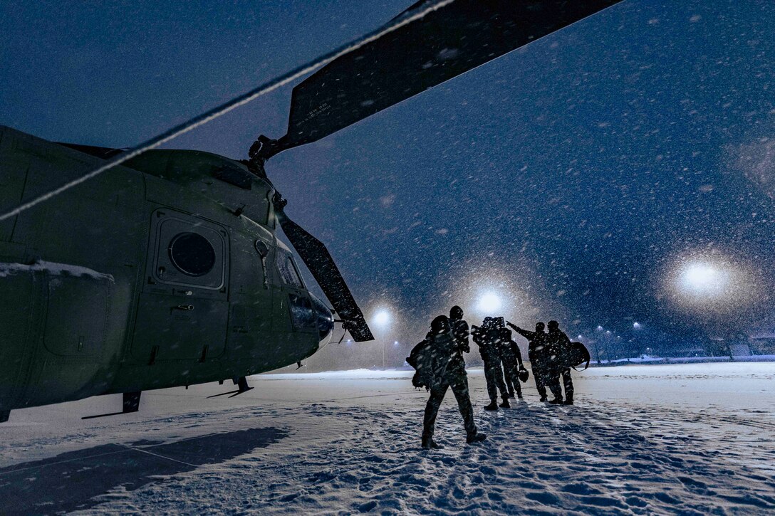 Soldiers walk next to a parked helicopter at night.