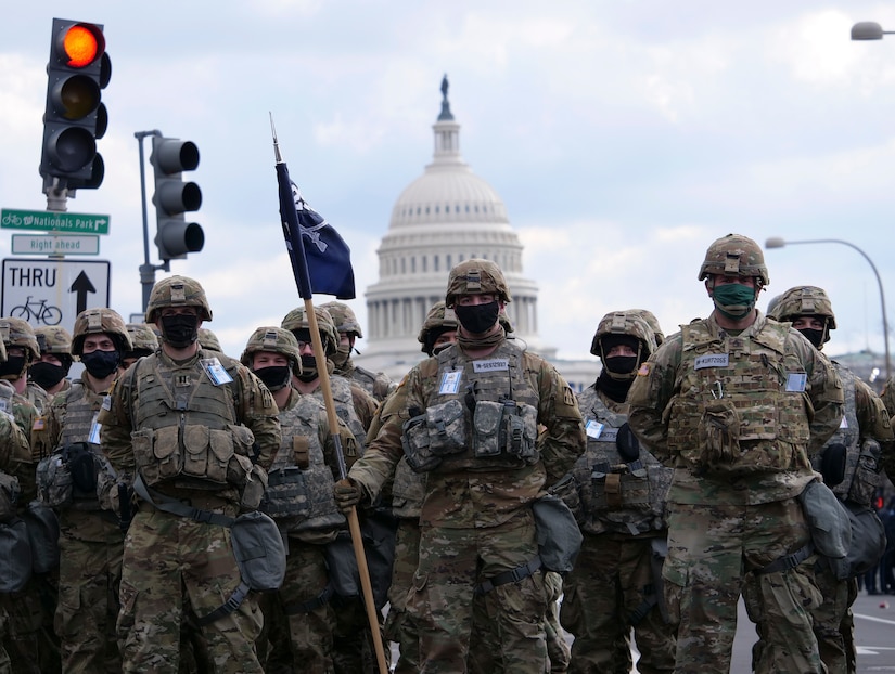 Multiple U.S. service members stand in a formation. The U.S. Capitol  is behind them.