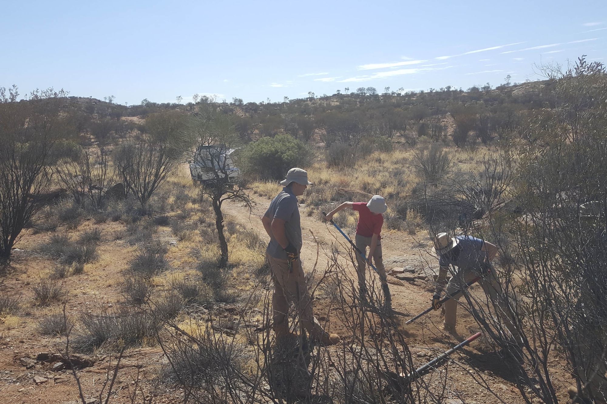 Paxton Rhoads (center), a 10th grade high school student at St. Philip's College in Alice Springs, Australia, assists Senior Airman Paul Wisniewski Jr. (left) and Tech. Sgt. Andrew Pauldine (right) as they distribute gravel and sand in washed-out sections of a trail leading to one of Detachment 421's seismic arrays.  Rhoads spent a week with the Airmen who maintain precision equipment used to detect nuclear explosions around the world.  (U.S. Air Force courtesy photo)