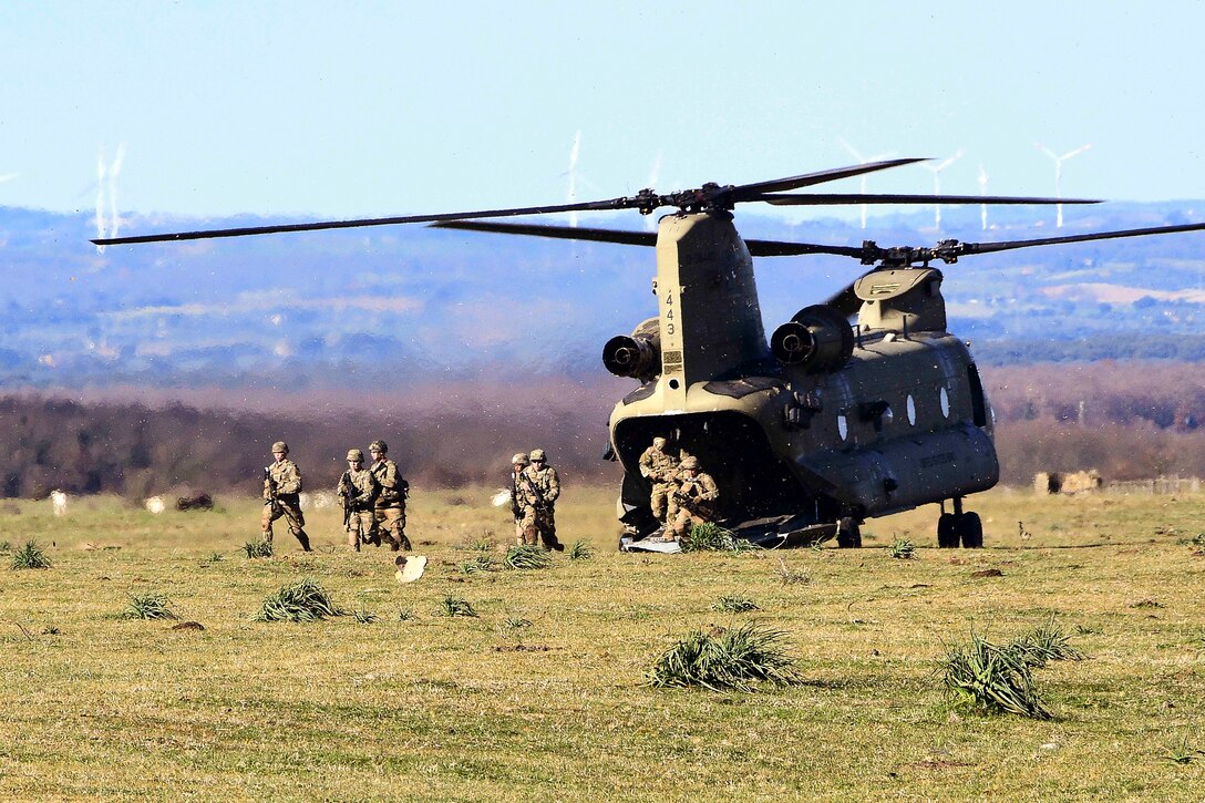 Soldiers exit a helicopter parked in a field.