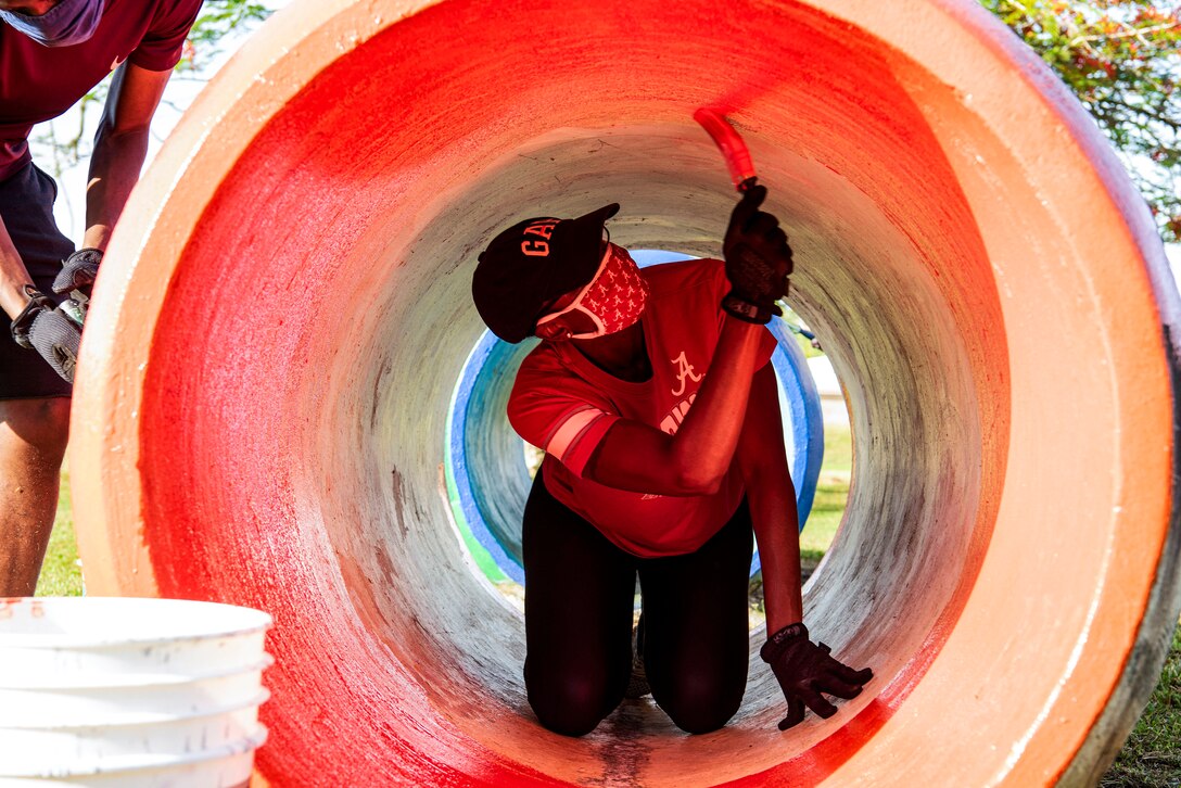 An airman in civilian clothes paints the inside of a tunnel pinkish-red.