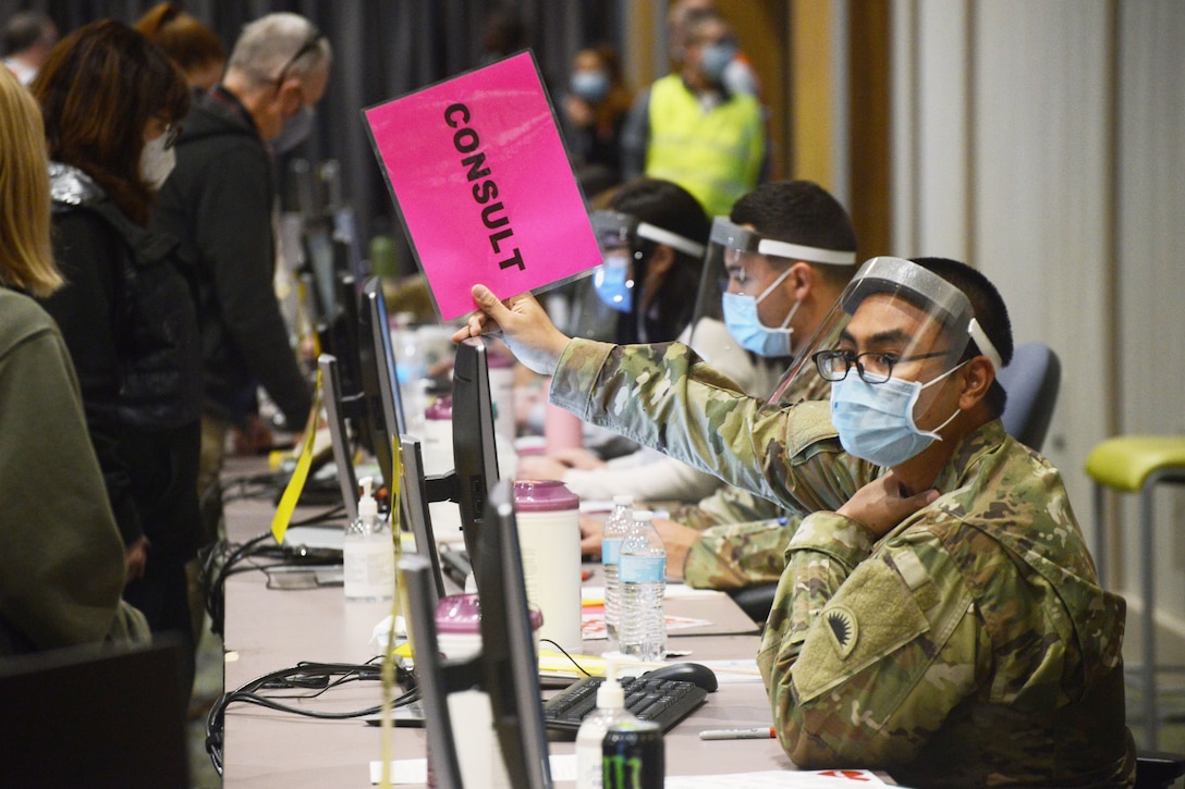 A guardsman wearing a face mask holds a pink placard t at a COVID-19 walk-in vaccination clinic.