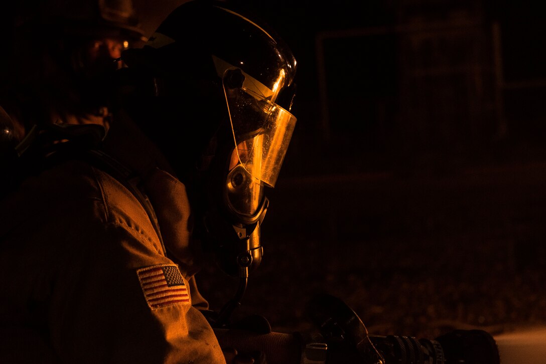 A firefighter stands with a hose putting out a simulated fire