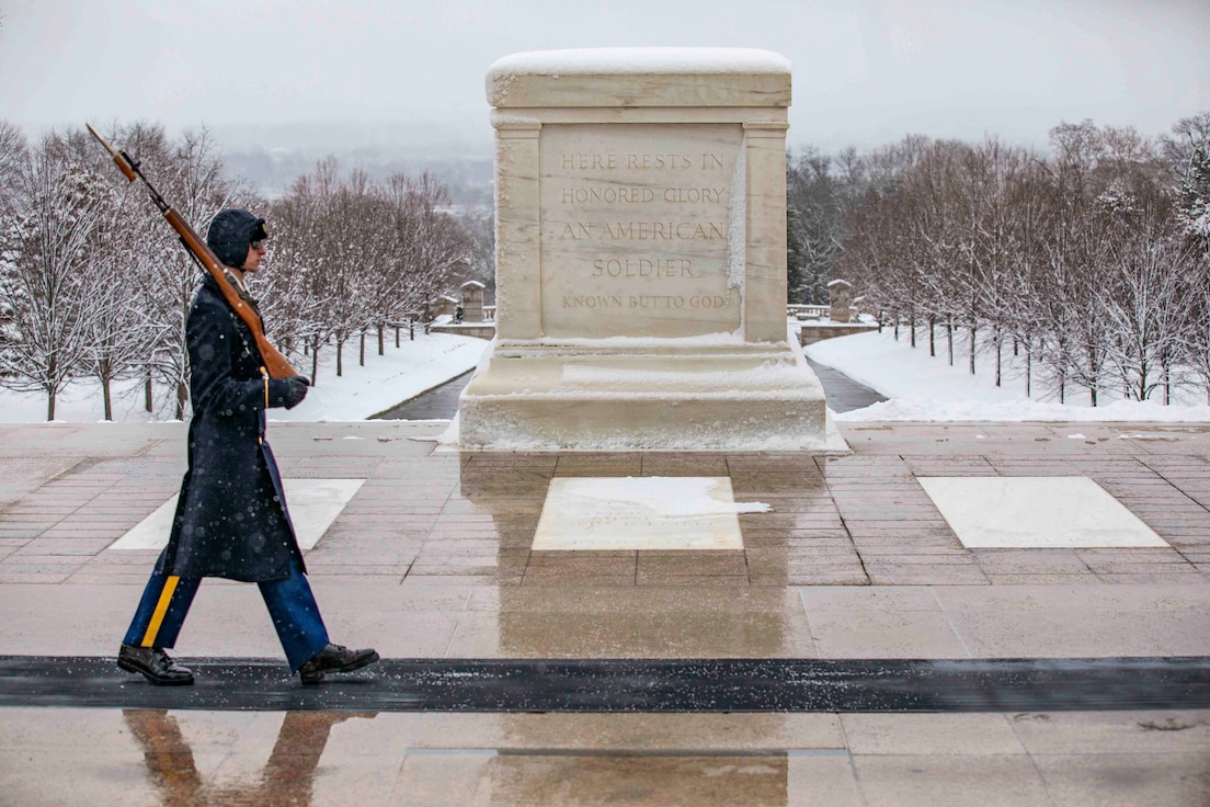 A soldier walks in the snow holding a rifle in front the Tomb of the Unknown Soldier.