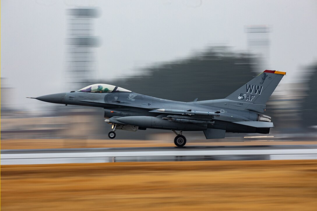 An F-16 takes off the flightline. The background is blurry and the photos are clear.
