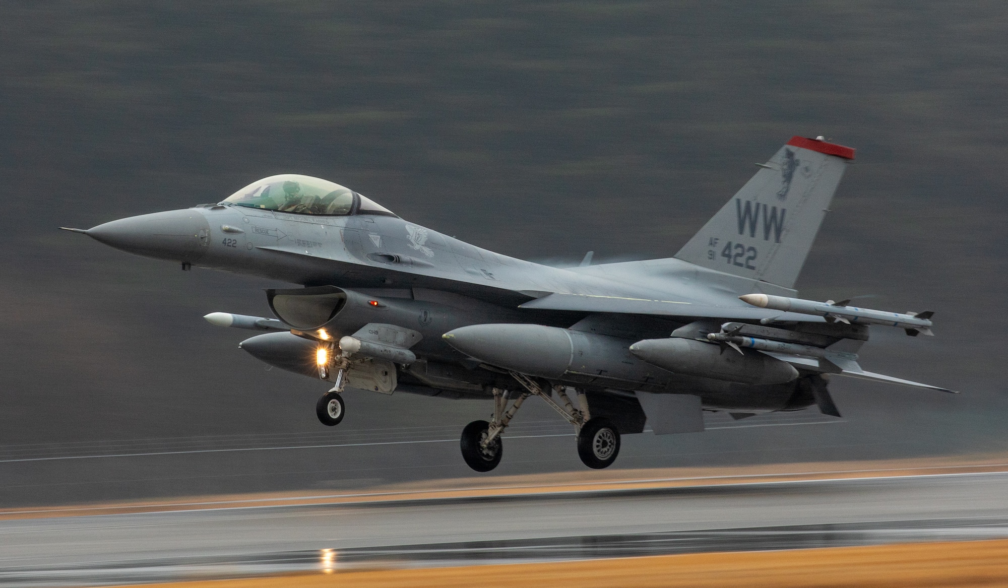An F-16 takes off from the flight line. The background is blurry and the subject is clear.