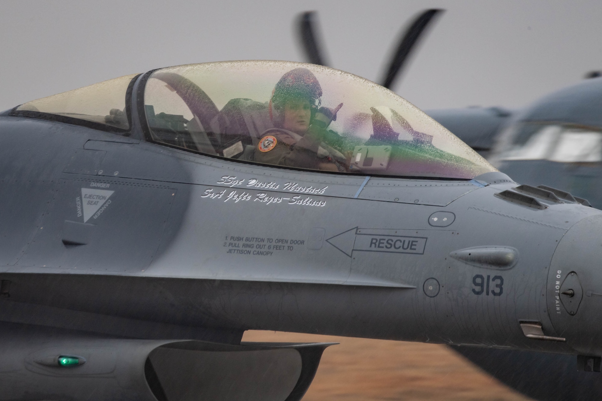 A pilot gestures with pinky and thumb extended from inside his canopy after landing.