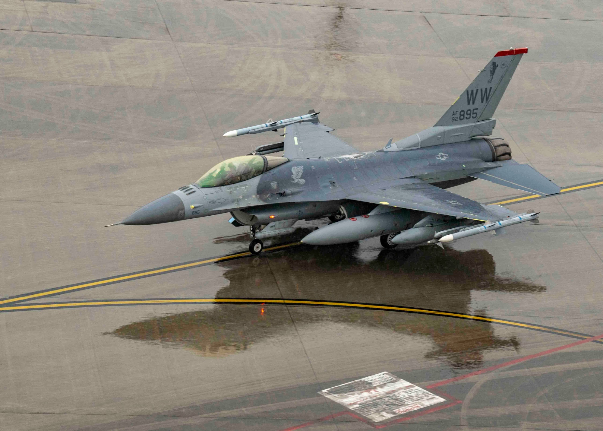 An F-16 sits on a rainy flightine. The photo is from top-down.