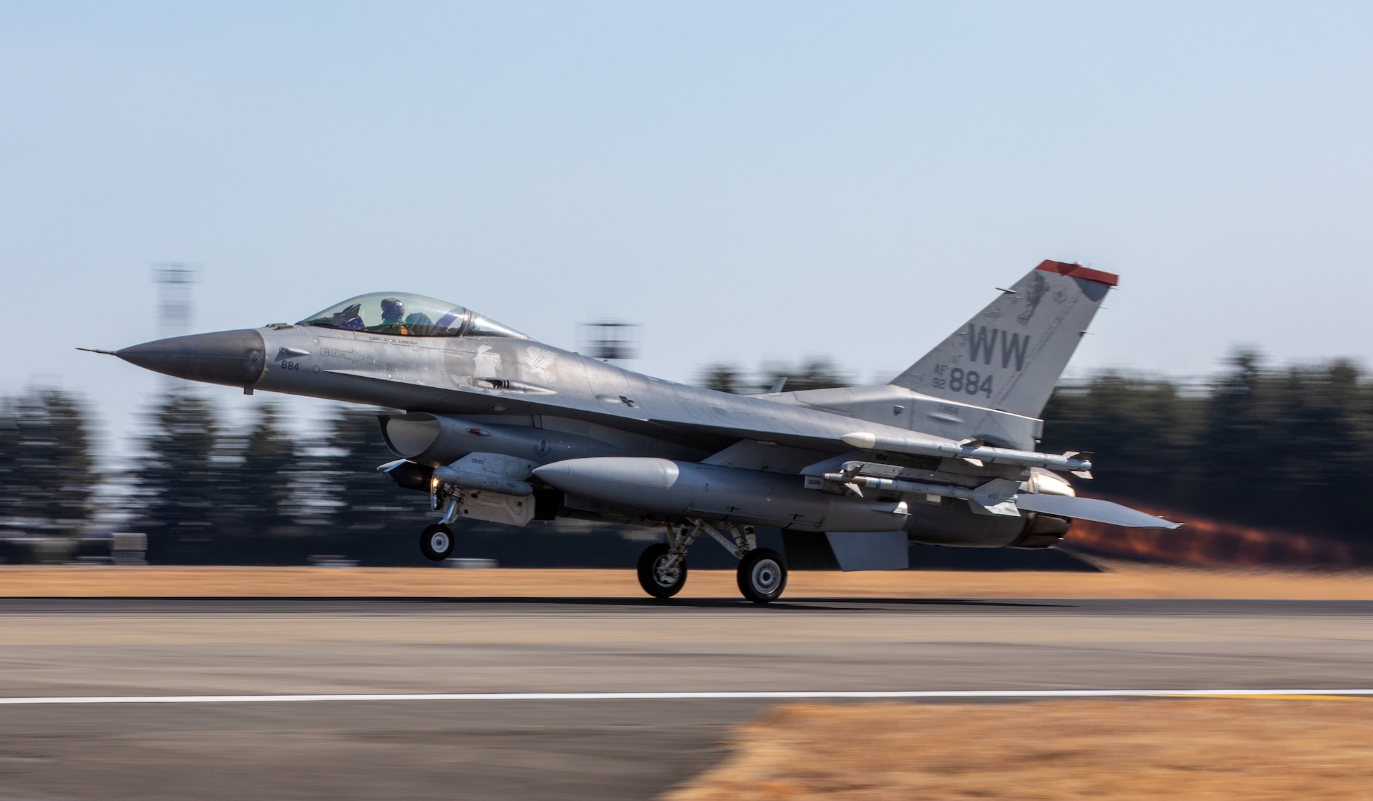 An F-16 Fighting Falcon takes off from the flightline. The photo is a side shot with a blurry background and sharp subject.
