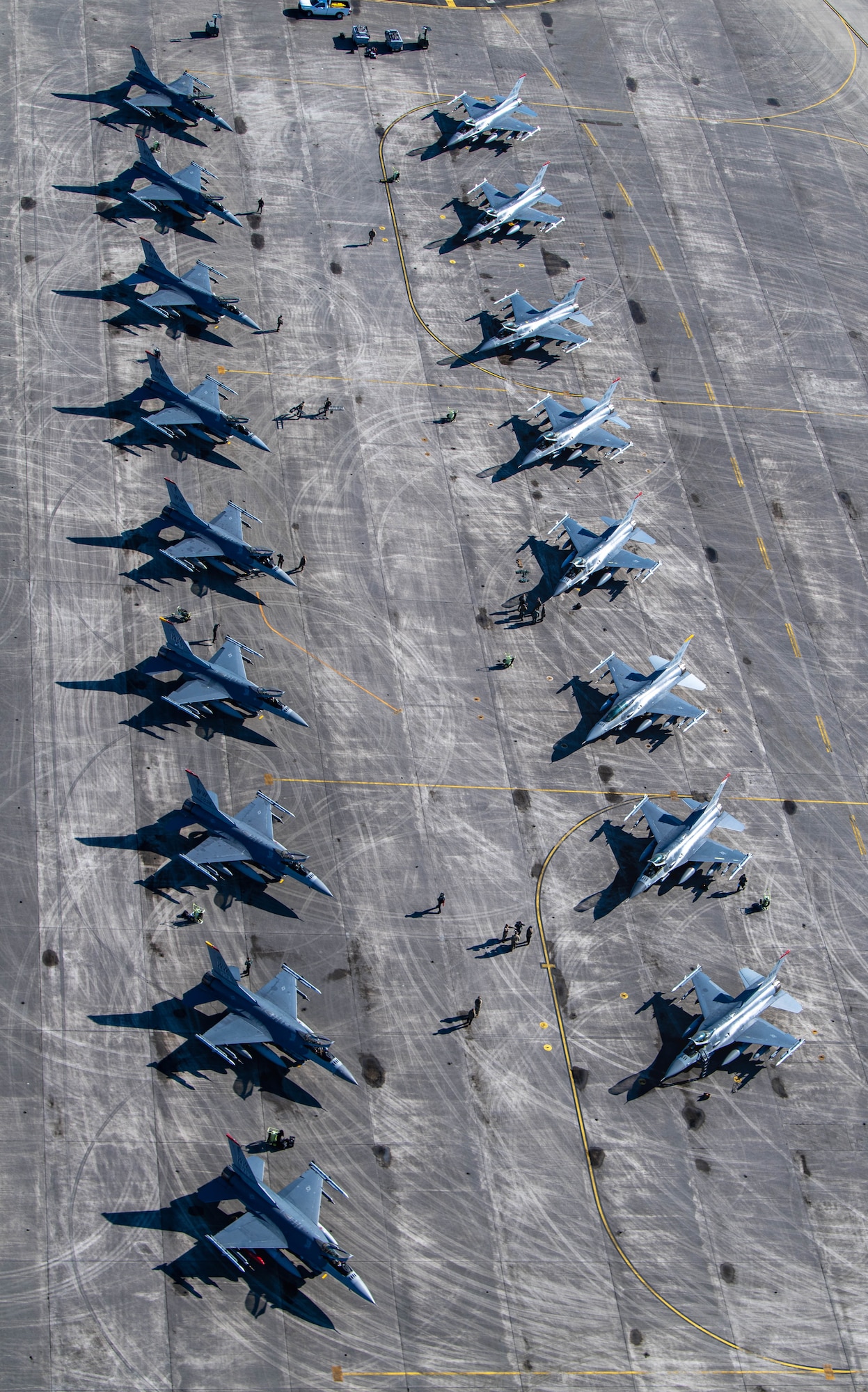 Top-down view of 15 F-16 Fighting Falcons sitting on a flightline in two rows.